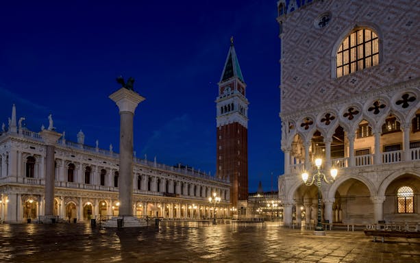 San Marco Square in Venice at night with illuminated buildings and bell tower.