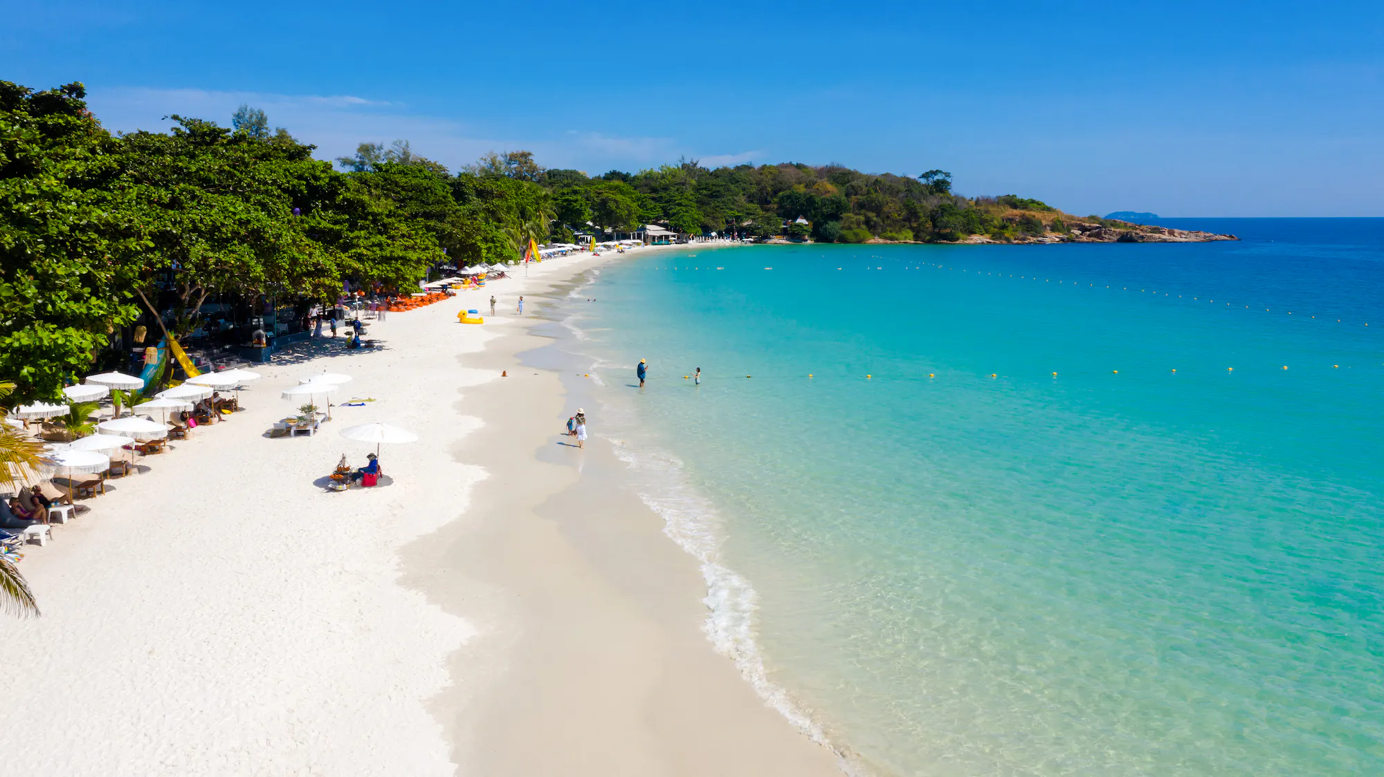 White sandy beach with umbrellas and people near turquoise water on Koh Samet Island, Thailand.