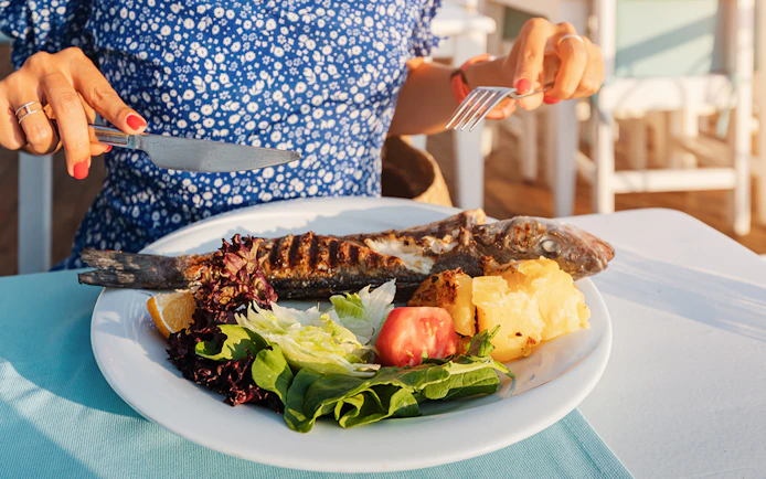 Grilled fish with salad and potatoes on a plate, Mediterranean lunch setting.