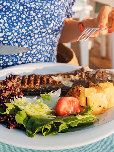 Grilled fish with salad and potatoes on a plate, Mediterranean lunch setting.