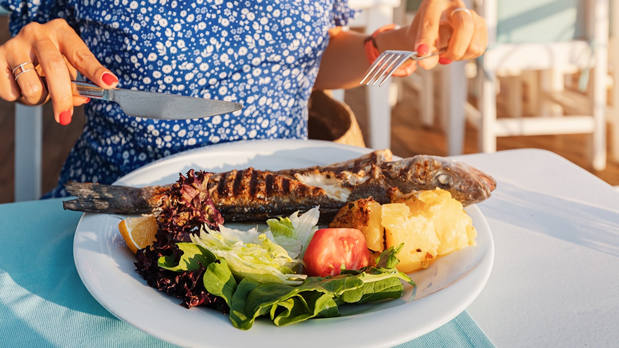 Grilled fish with salad and potatoes on a plate, Mediterranean lunch setting.