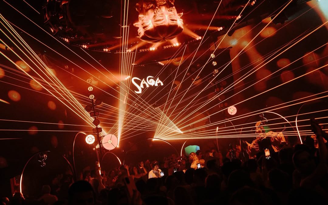 DJ performing at Club Chinois during SAGA event, Ibiza, with vibrant light show.
