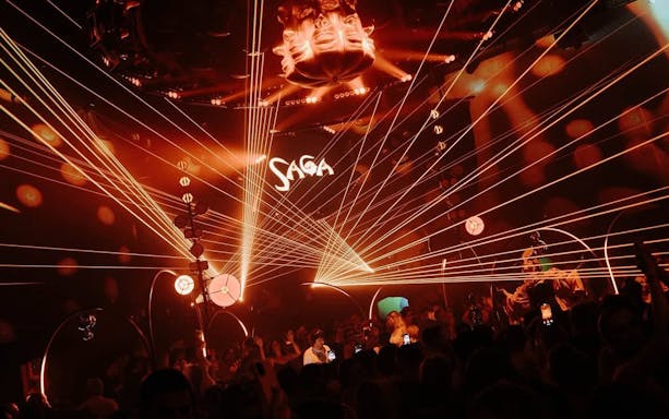 DJ performing at Club Chinois during SAGA event, Ibiza, with vibrant light show.