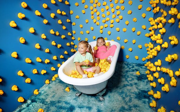 Children in a bathtub filled with rubber ducks at Bubble Planet Atlanta exhibit.