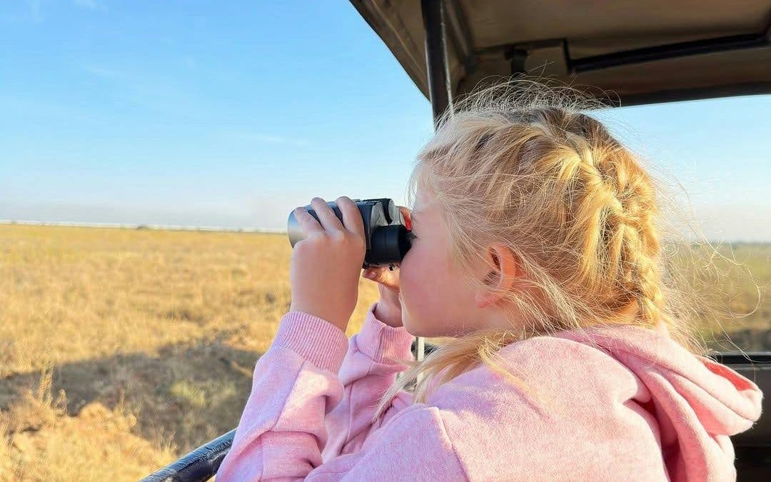 Child observing wildlife with binoculars on Nairobi National Park safari.