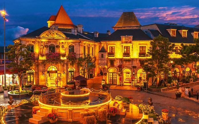 Central square in medieval French village at Ba Na Hills Park, Da Nang, illuminated at dusk.