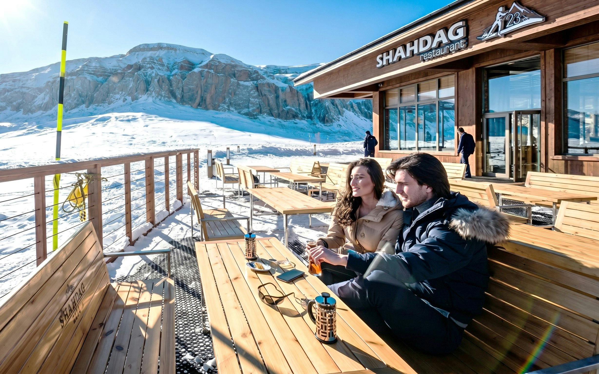 Couple enjoying drinks on Shahdag Mountain Resort terrace with snowy mountains in Baku.