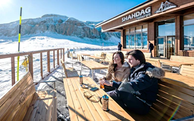 Couple enjoying drinks on Shahdag Mountain Resort terrace with snowy mountains in Baku.