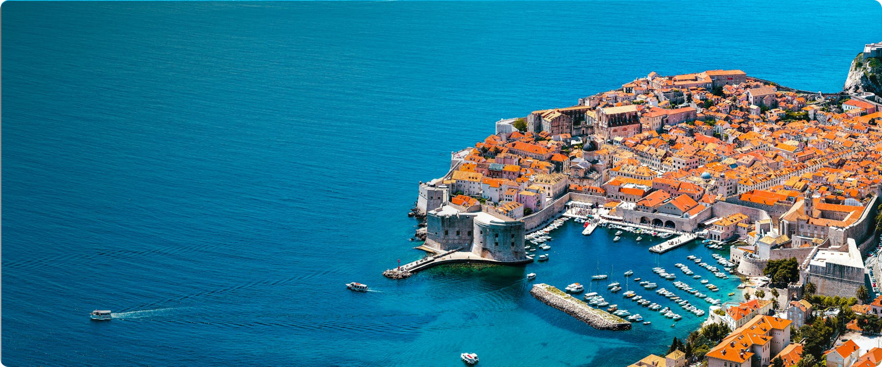 Aerial view of Dubrovnik's Old Town with city walls and boats in the Adriatic Sea.