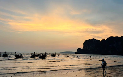 Longtail boats on Railay Beach at sunset, Krabi, with limestone cliffs in the background.
