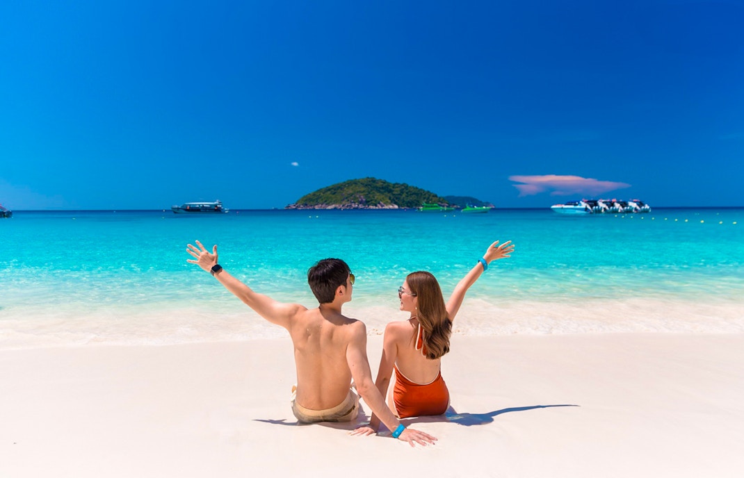 Couple enjoying Similan Islands beach with speedboats in turquoise water, Phuket tour.