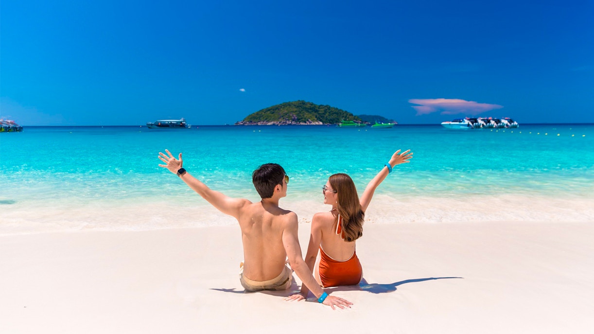 Couple enjoying Similan Islands beach with speedboats in turquoise water, Phuket tour.