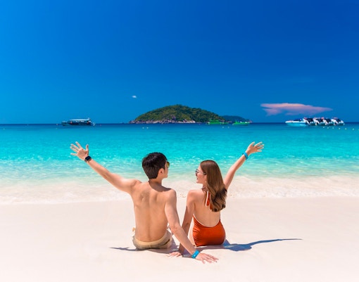 Couple enjoying Similan Islands beach with speedboats in turquoise water, Phuket tour.
