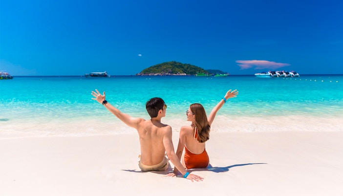 Couple enjoying Similan Islands beach with speedboats in turquoise water, Phuket tour.