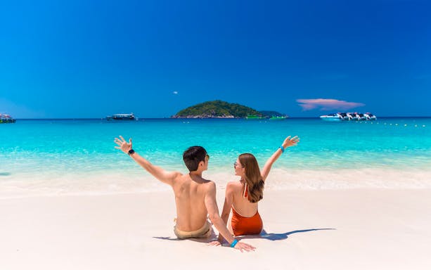 Couple enjoying Similan Islands beach with speedboats in turquoise water, Phuket tour.