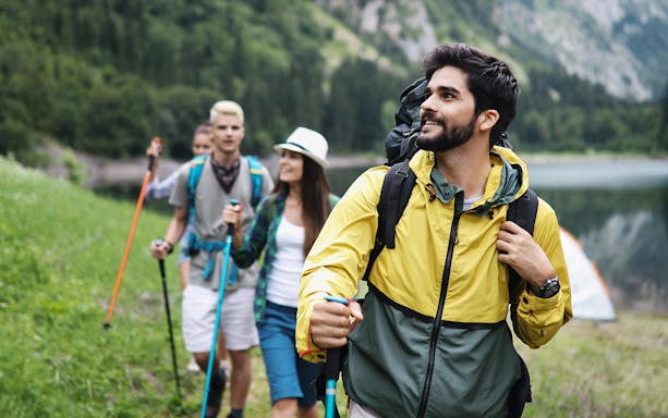 Friends hiking on a trail near a lake with mountains in the background.