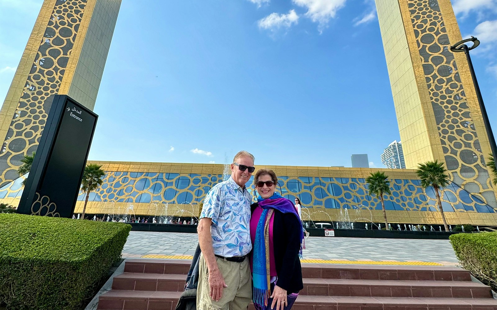 Couple standing in front of the Dubai Frame with decorative patterns and clear sky.