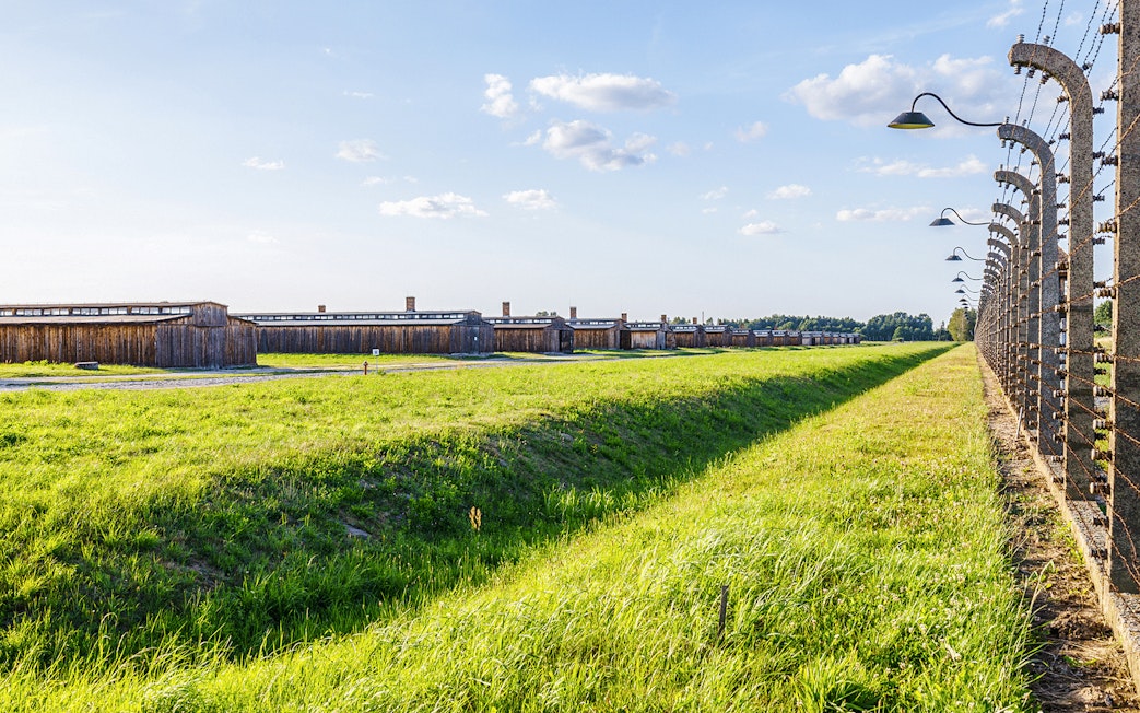 Auschwitz II barracks and barbed wire fences under a clear sky.