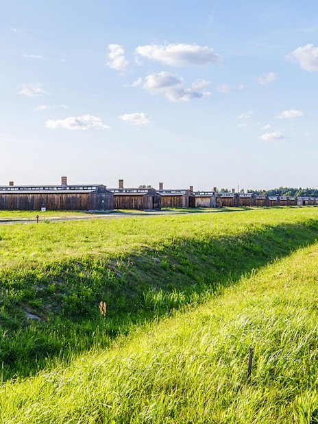 Auschwitz II barracks and barbed wire fences under a clear sky.