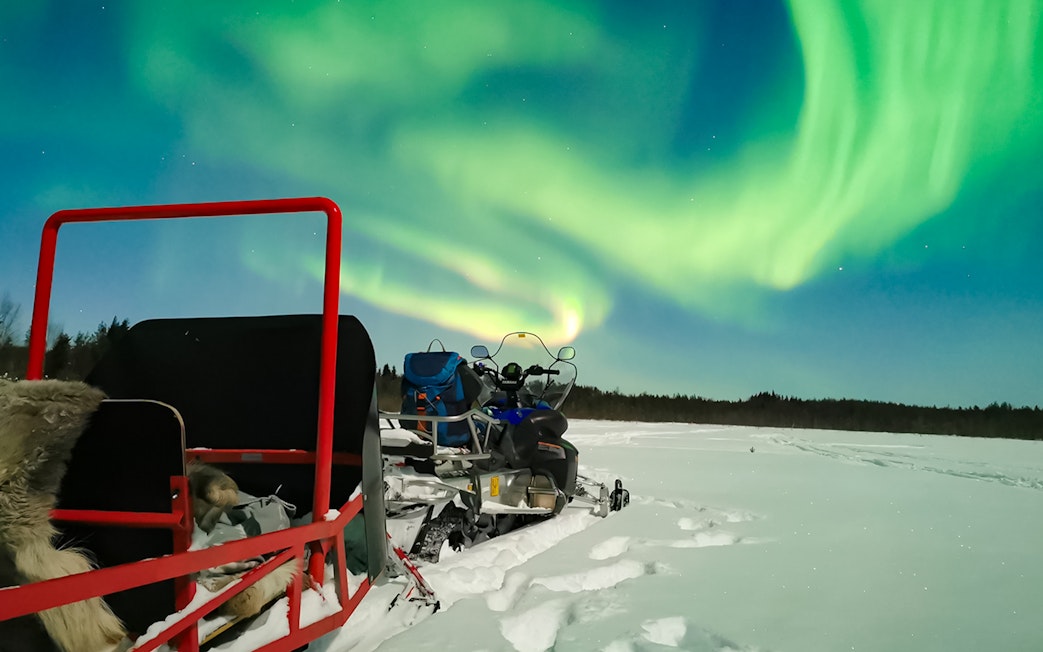 Snowmobile and sled under Northern Lights in Levi, Finland.