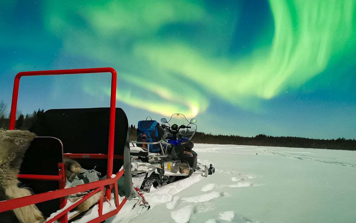 Snowmobile and sled under Northern Lights in Levi, Finland.
