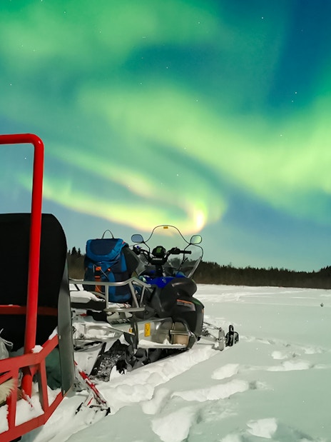 Snowmobile and sled under Northern Lights in Levi, Finland.