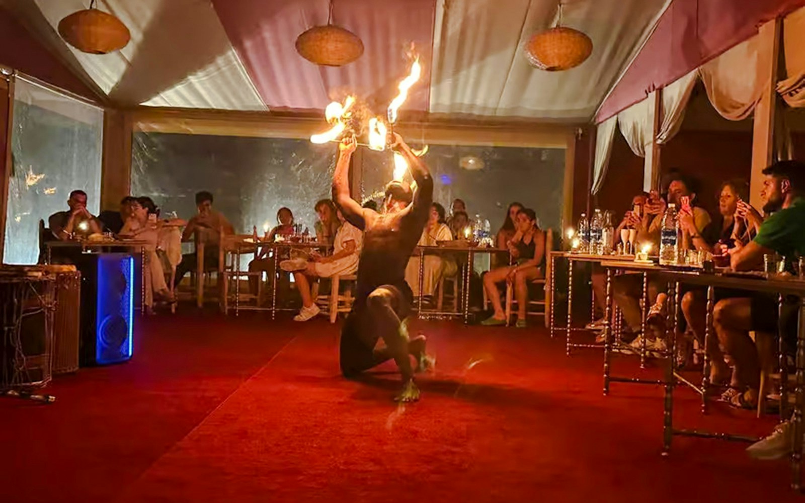 Performer with fire in Marrakech desert camp Agafay, audience watching.
