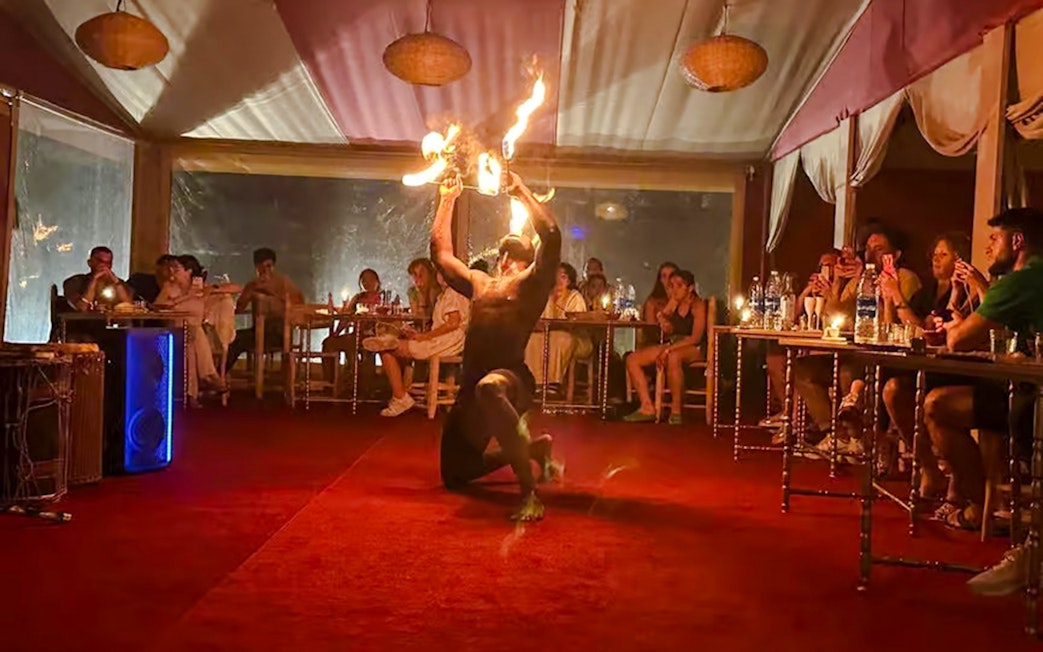 Performer with fire in Marrakech desert camp Agafay, audience watching.