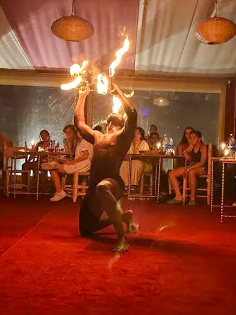 Performer with fire in Marrakech desert camp Agafay, audience watching.