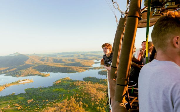 Hot air balloon over Brisbane landscape with passengers enjoying the view.