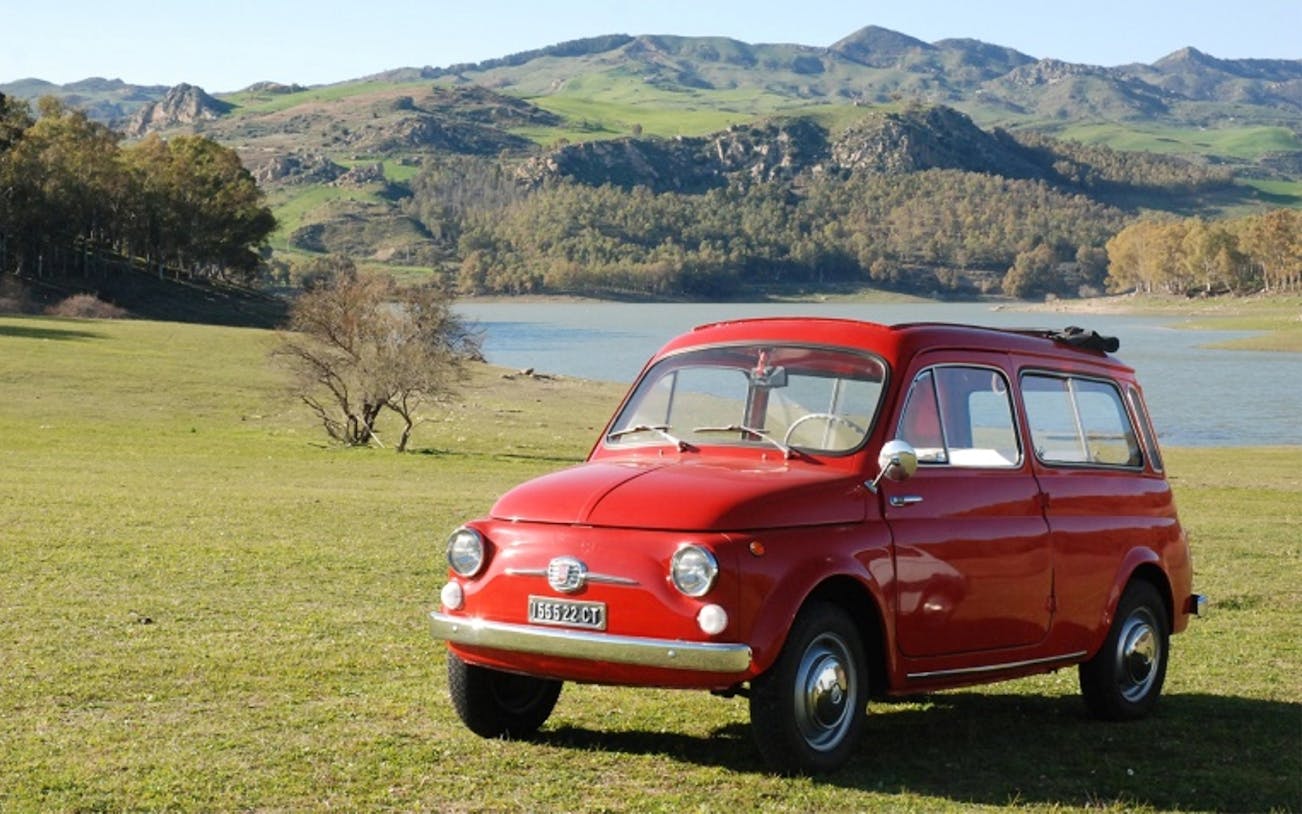 Vintage red car parked by a scenic lake in Sicily, part of The Godfather Tour from Catania.