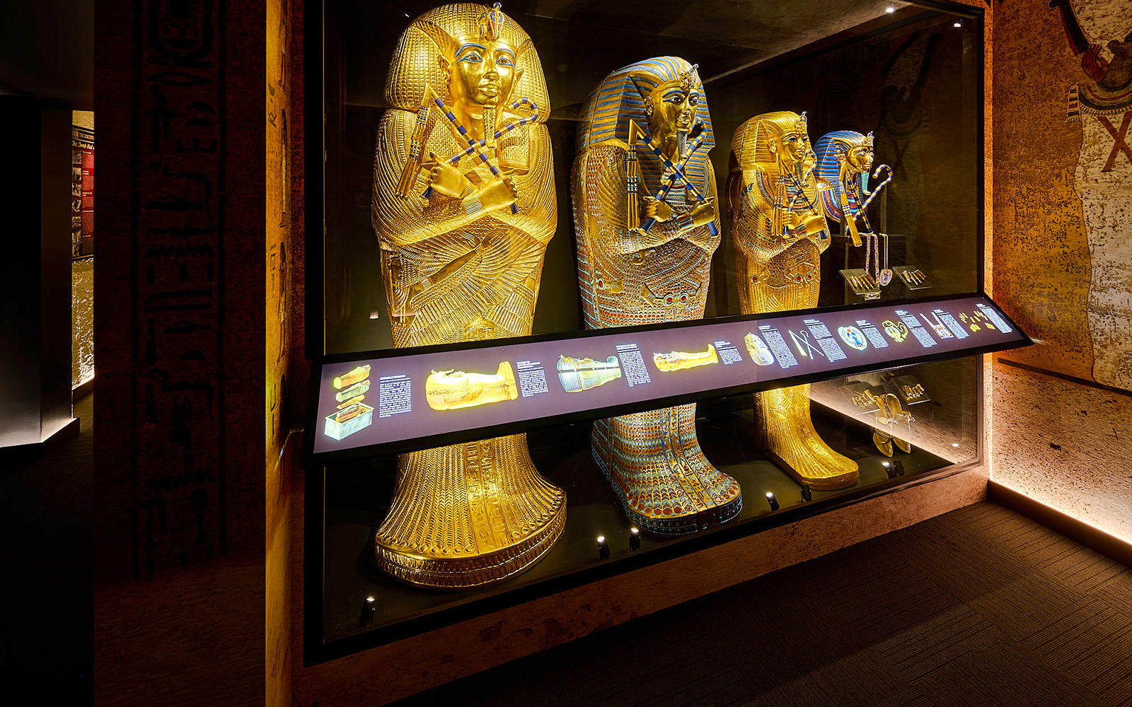 Golden sarcophagi of pharaohs in a museum display case with informational panel.
