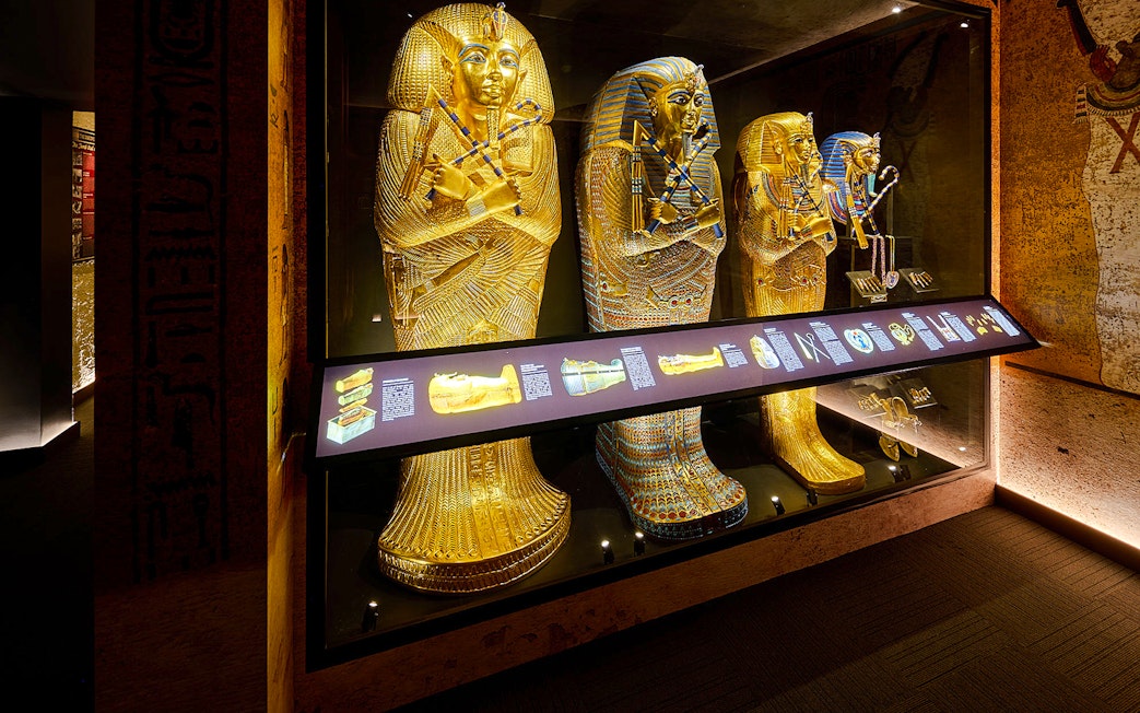 Golden sarcophagi of pharaohs in a museum display case with informational panel.