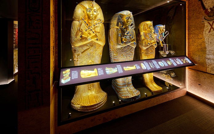 Golden sarcophagi of pharaohs in a museum display case with informational panel.