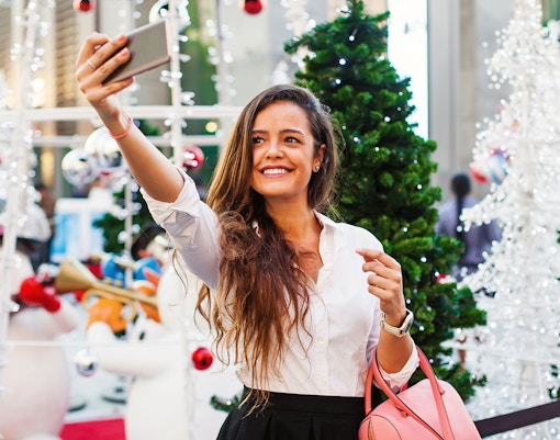 Woman taking a selfie at Winter City, Expo City with festive decorations and Christmas trees.