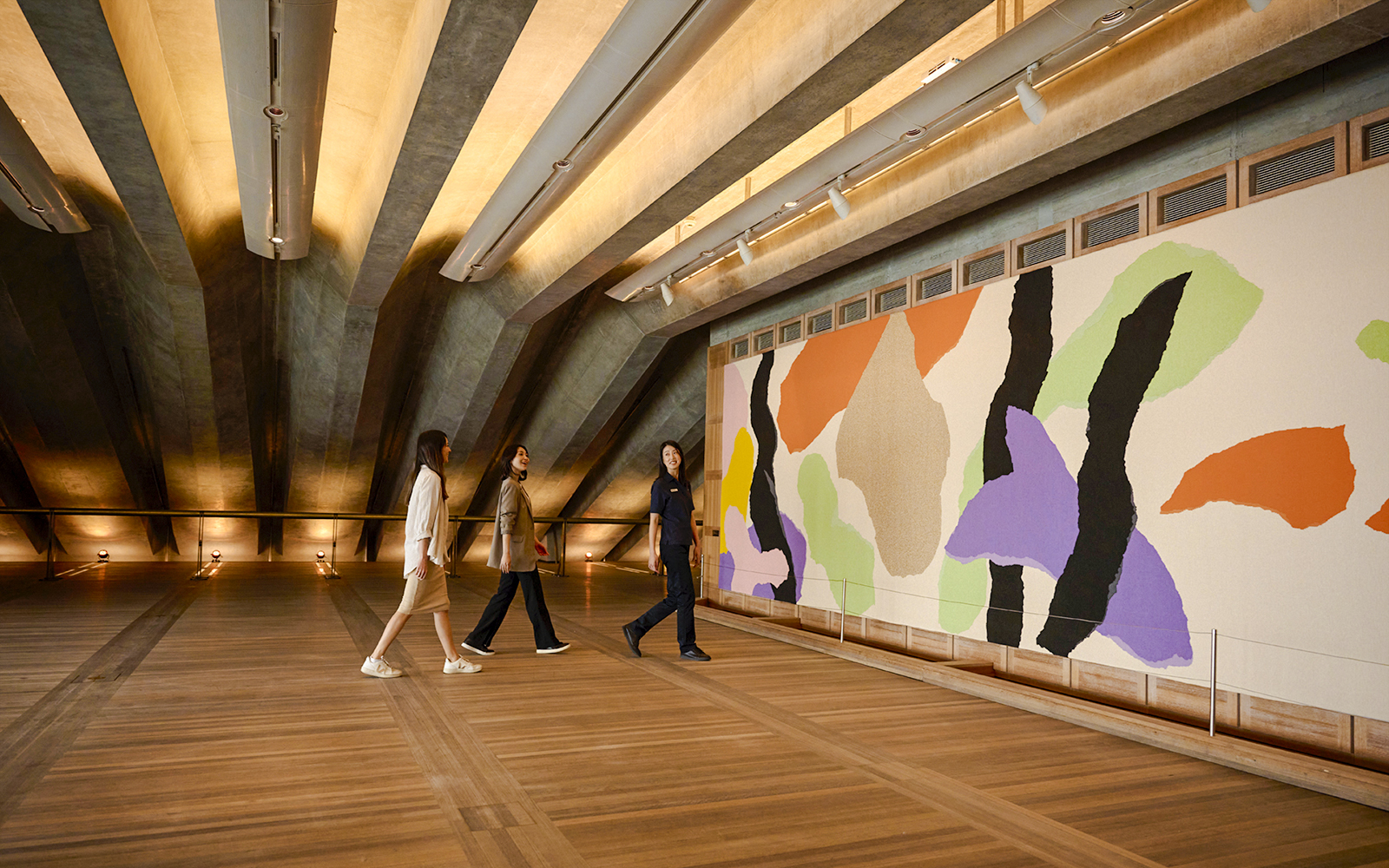 People on a guided tour in the Utzon Room, Sydney Opera House, viewing colorful wall art.