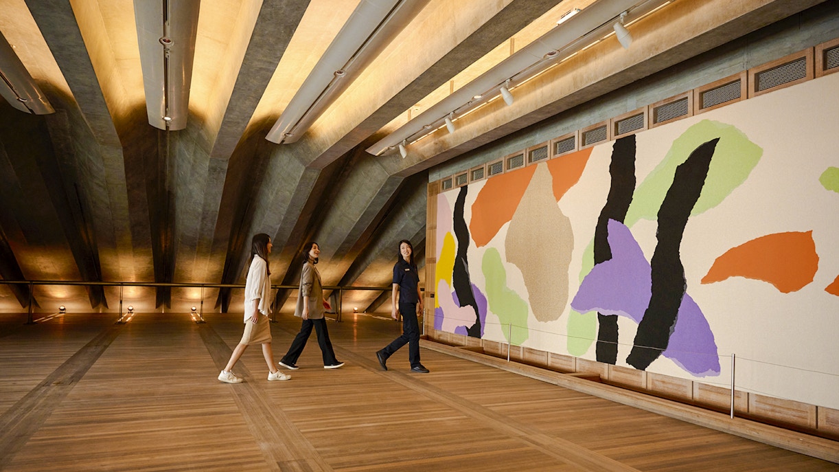 People on a guided tour in the Utzon Room, Sydney Opera House, viewing colorful wall art.
