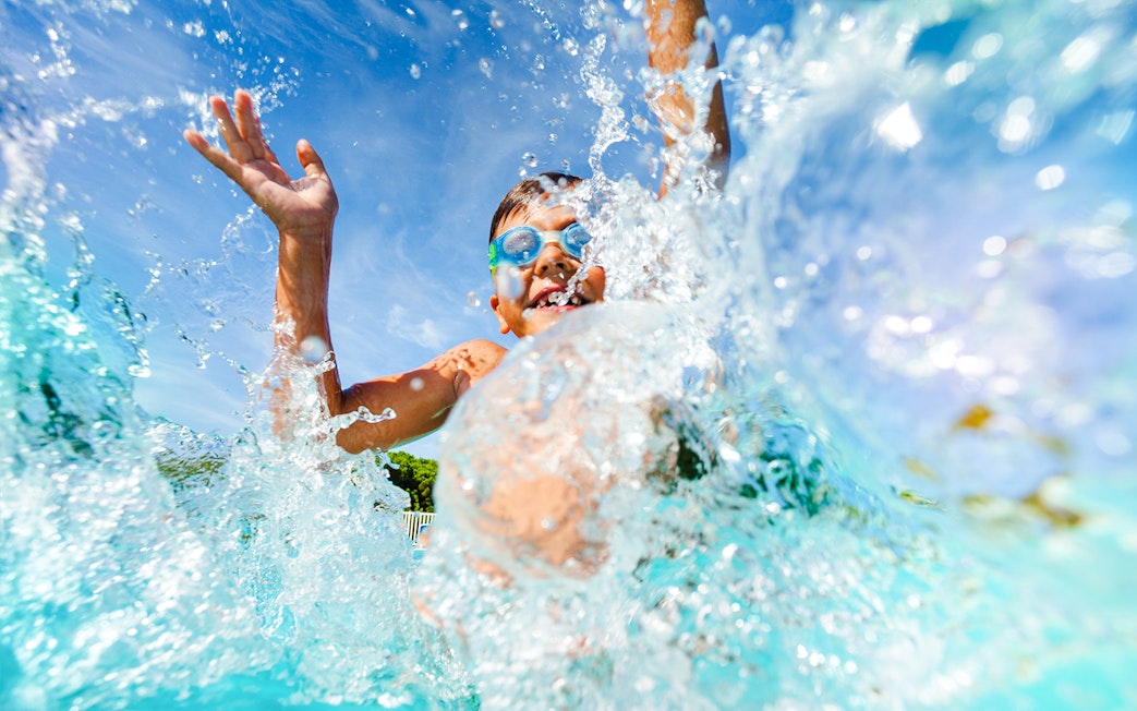Young boy splashing in water at a water park, wearing goggles.