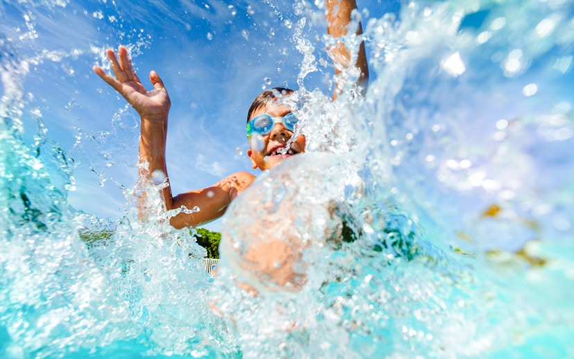 Young boy splashing in water at a water park, wearing goggles.