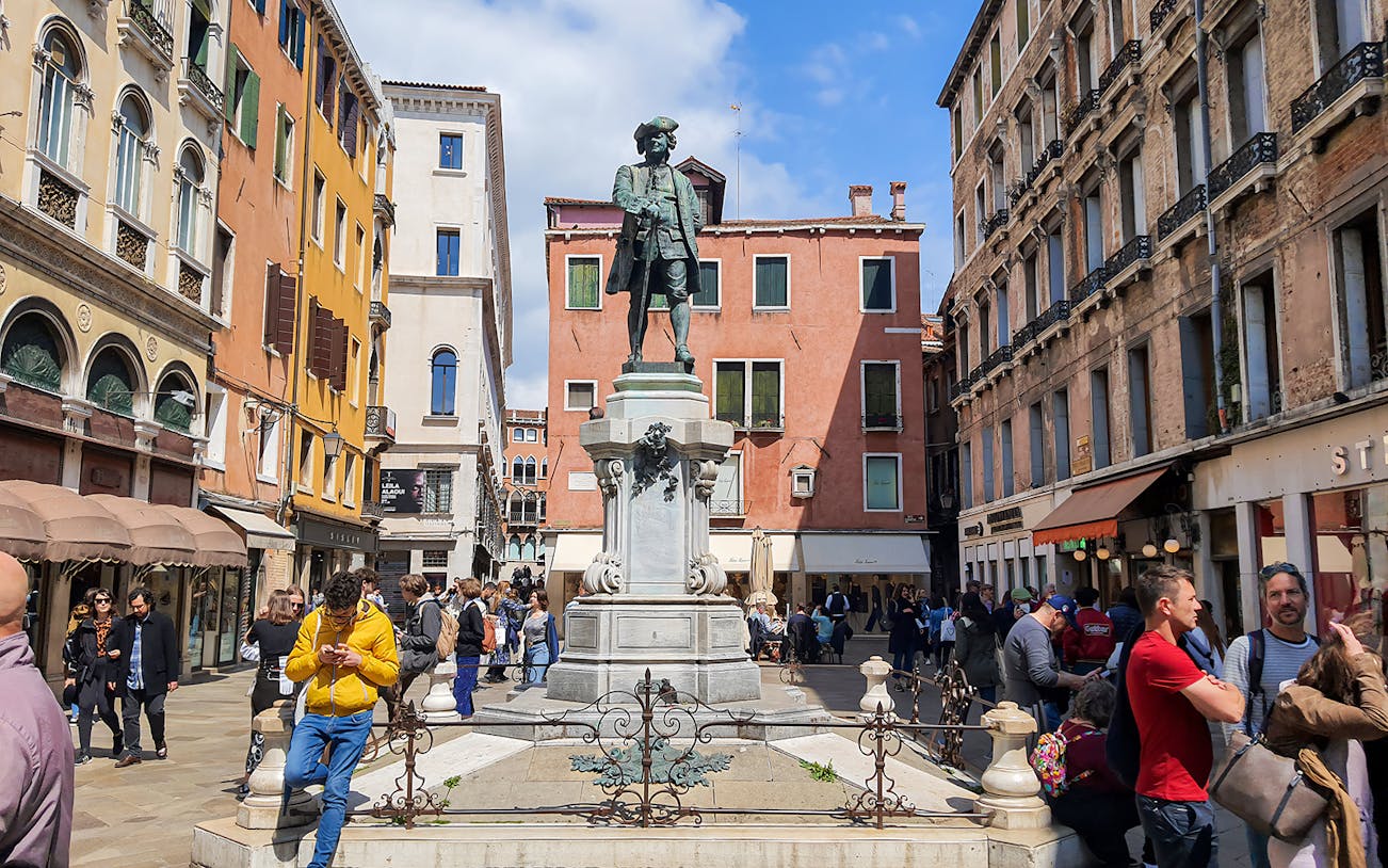 Statue of Carlo Goldoni in a bustling Venetian square, part of a guided culinary and sightseeing tour.