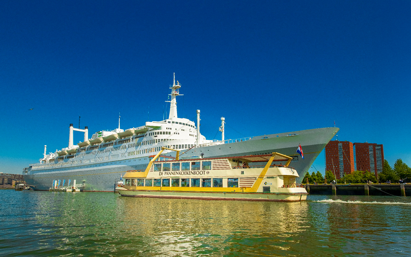 Pancake Cruise boat sailing near a large ship in Rotterdam harbor.