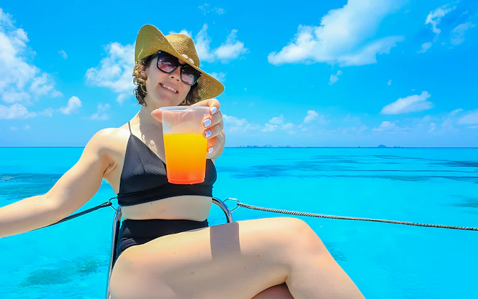 Person relaxing on a catamaran with a drink, sailing from Cancun to Isla Mujeres.