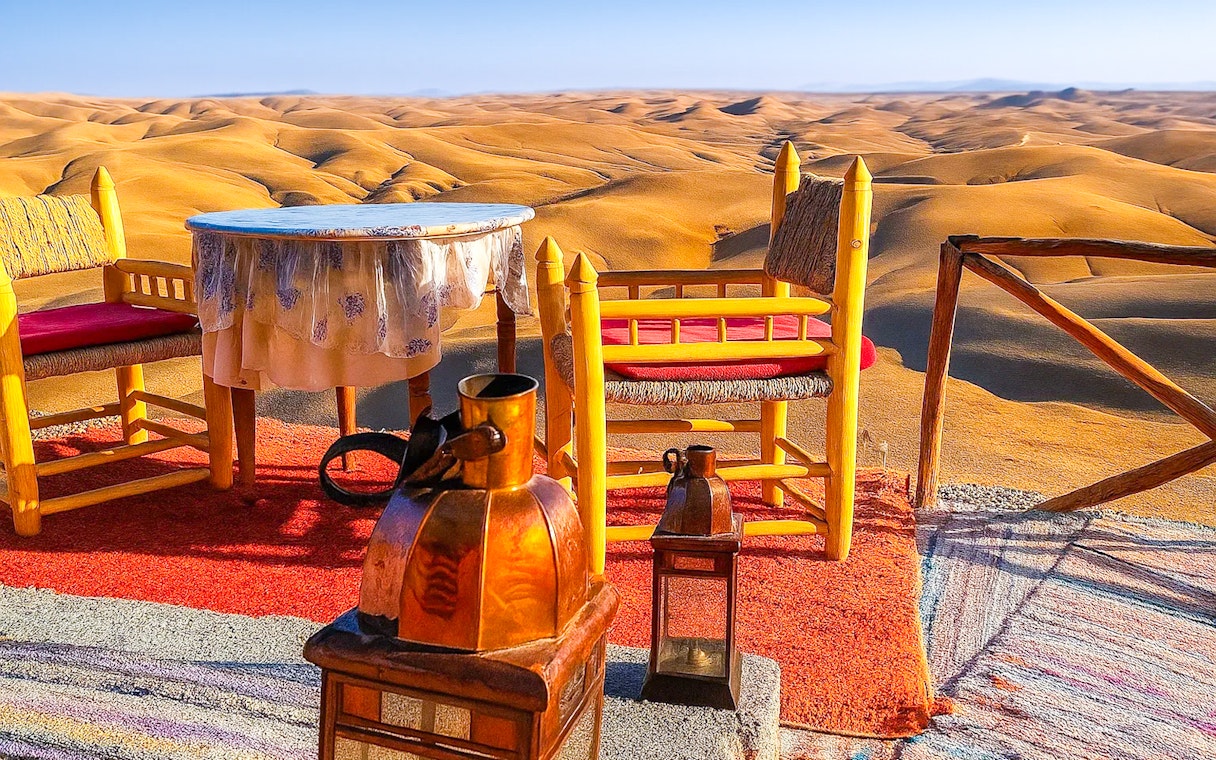 Desert camp setup with chairs and table overlooking Agafay Desert dunes near Marrakech.