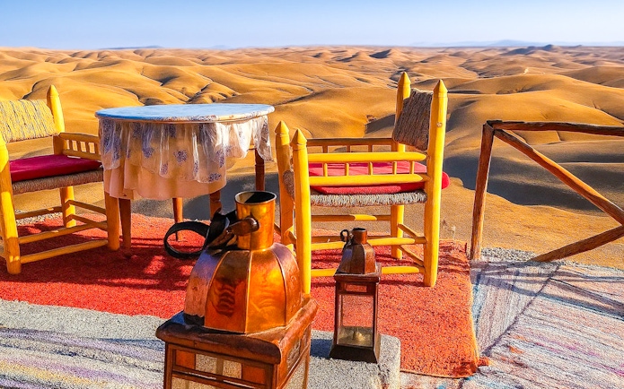 Desert camp setup with chairs and table overlooking Agafay Desert dunes near Marrakech.