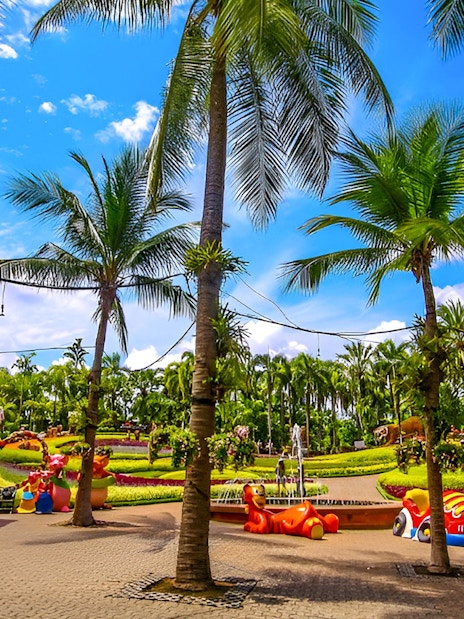Nong Nooch Tropical Garden with palm trees and colorful sculptures in Pattaya, Thailand.