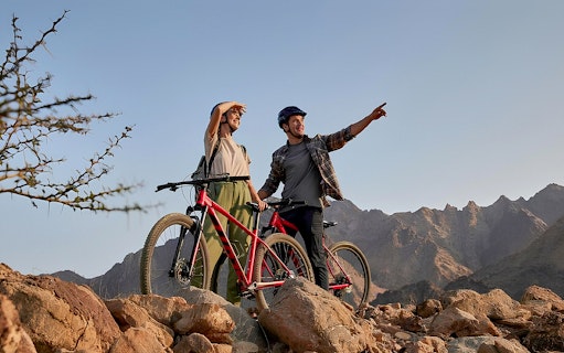 Mountain bikers pointing at Hatta mountains during a tour.