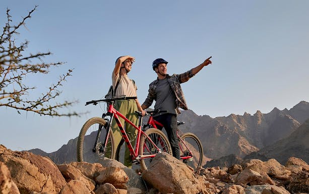 Mountain bikers pointing at Hatta mountains during a tour.