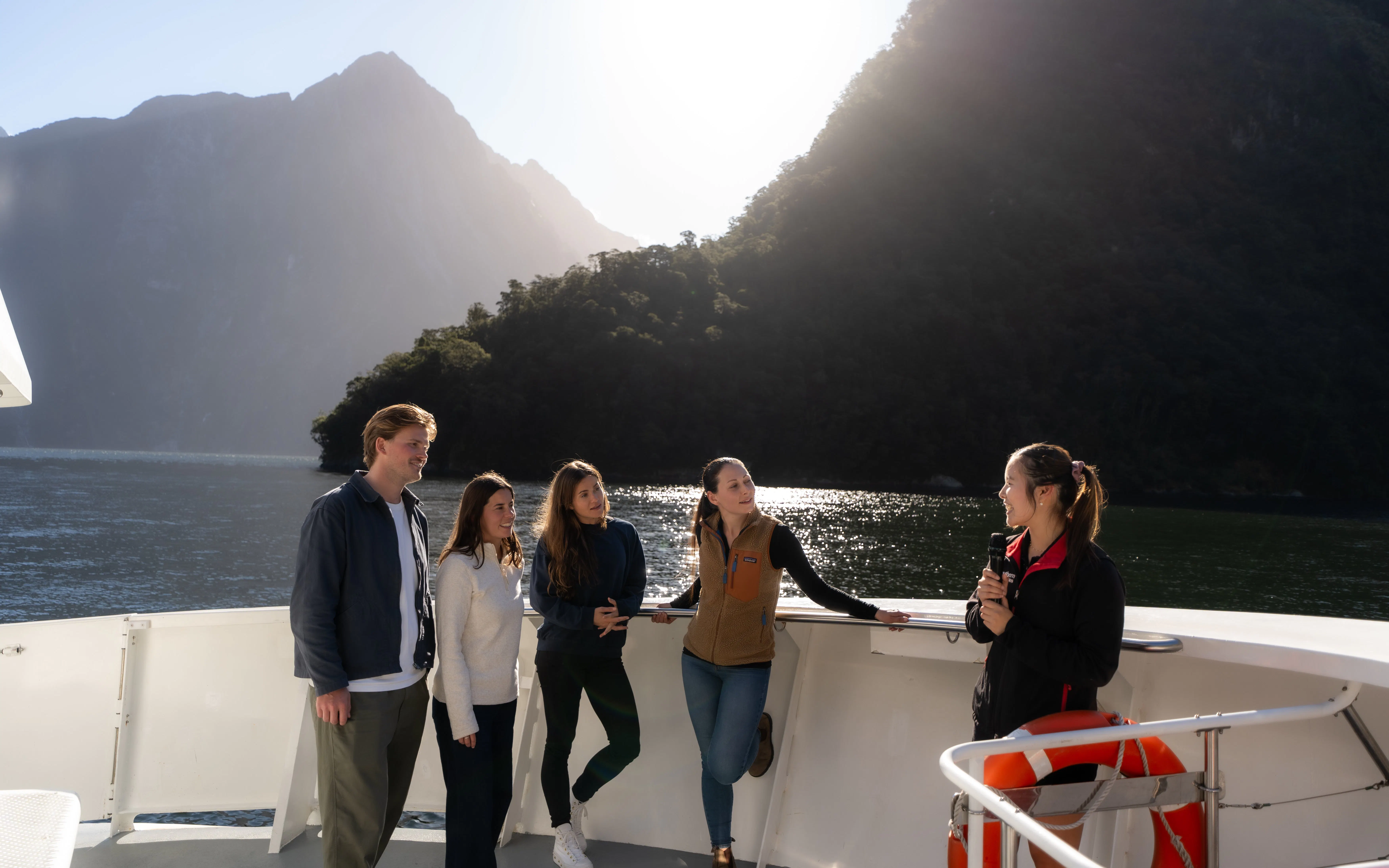 Tour group on Milford Sound cruise with guide, surrounded by mountains and water.