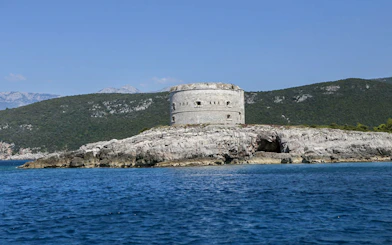 Old fort on rocky island in Boka Bay, Montenegro, with mountains in the background.