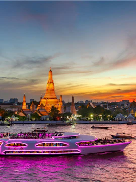 Wat Arun temple and illuminated cruise ship at twilight in Bangkok, Thailand.